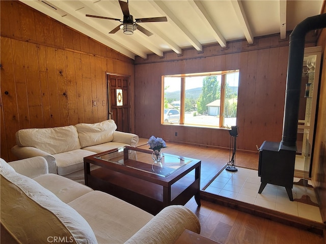 living room featuring vaulted ceiling with beams, light hardwood / wood-style floors, ceiling fan, and a wood stove