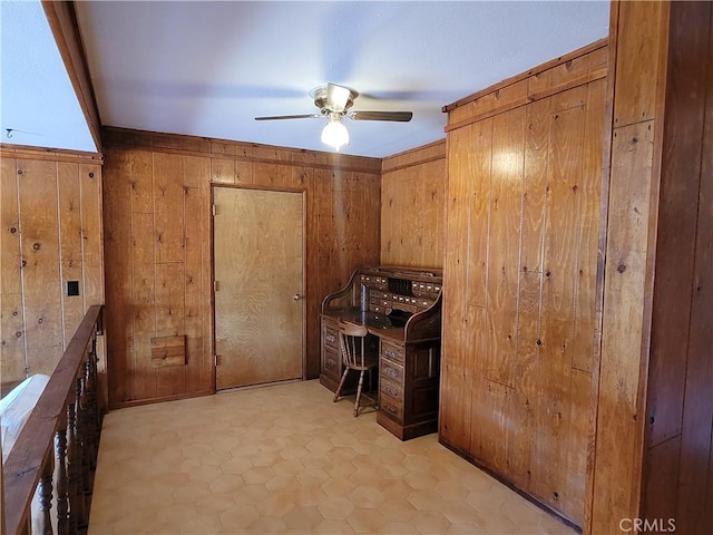 office space with light tile patterned flooring, ceiling fan, and wood walls