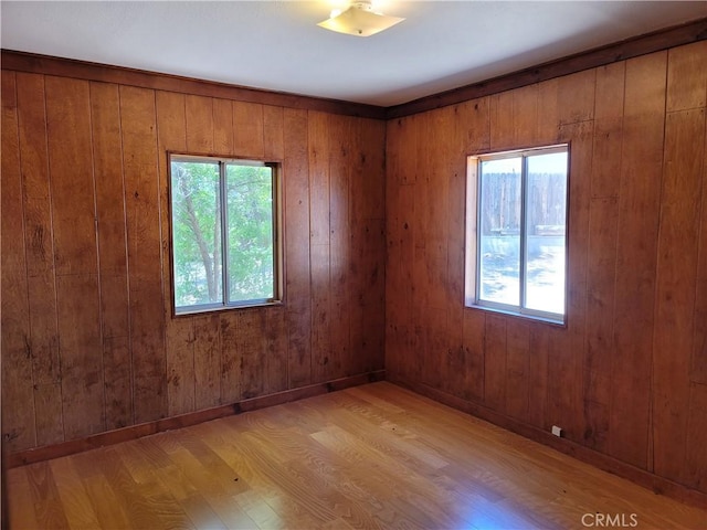 empty room with plenty of natural light, wooden walls, and light wood-type flooring