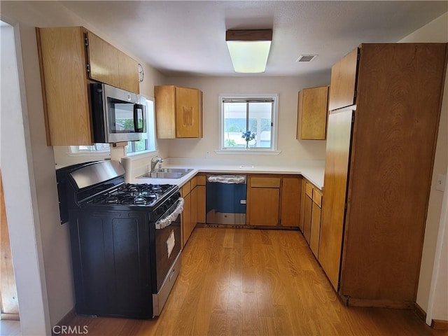 kitchen with appliances with stainless steel finishes, sink, and light hardwood / wood-style flooring