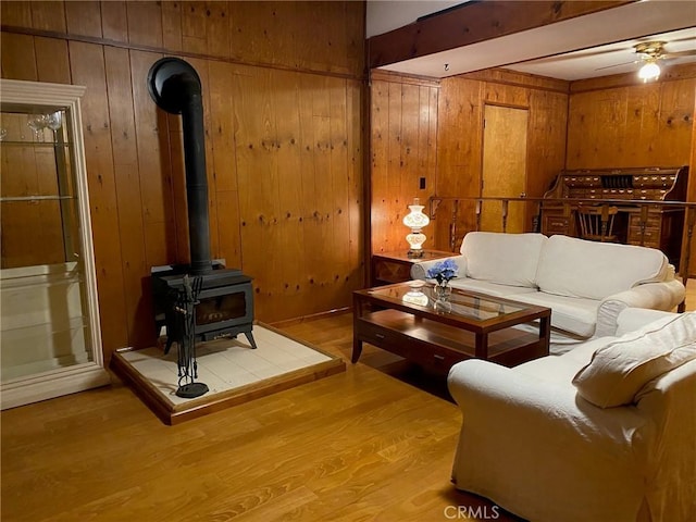 living room featuring hardwood / wood-style flooring, wood walls, ceiling fan, and a wood stove