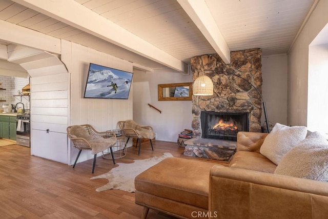 living room with beamed ceiling, a stone fireplace, wood-type flooring, and wood ceiling