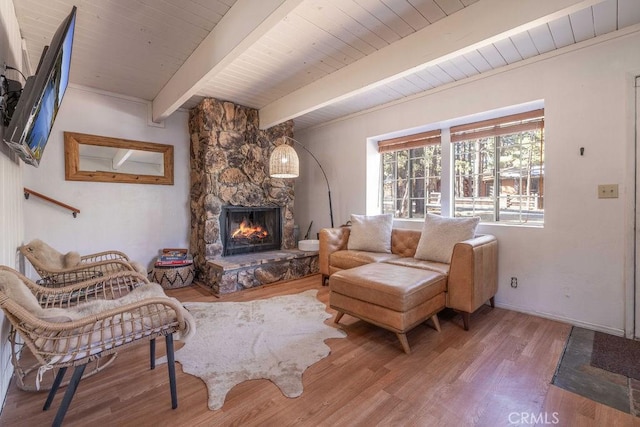 living room featuring beam ceiling, hardwood / wood-style flooring, a stone fireplace, and wooden ceiling