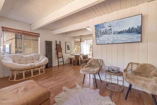 living room with beam ceiling, wooden ceiling, a notable chandelier, wood-type flooring, and wooden walls