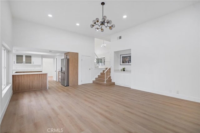 unfurnished living room with an inviting chandelier, a high ceiling, and light wood-type flooring