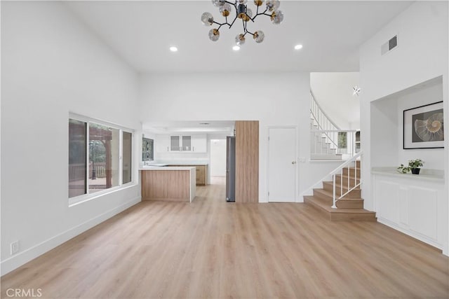 unfurnished living room with a notable chandelier, a towering ceiling, and light hardwood / wood-style flooring