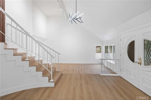 entrance foyer with an inviting chandelier, light hardwood / wood-style floors, track lighting, and high vaulted ceiling