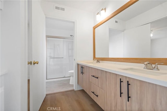 bathroom featuring vanity, a shower with door, ceiling fan, wood-type flooring, and toilet