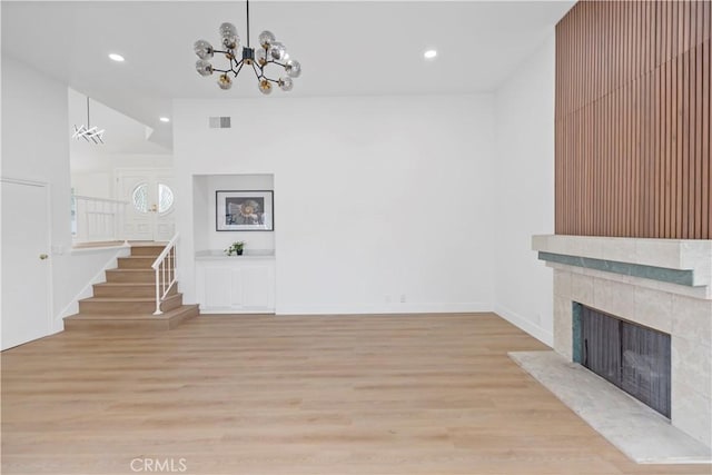 unfurnished living room with a tile fireplace, a towering ceiling, light wood-type flooring, and an inviting chandelier