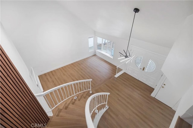 stairs featuring a chandelier, wood-type flooring, and vaulted ceiling