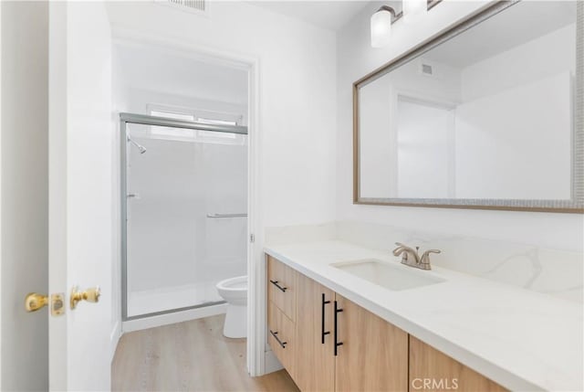 bathroom with hardwood / wood-style flooring, vanity, toilet, and a shower with door