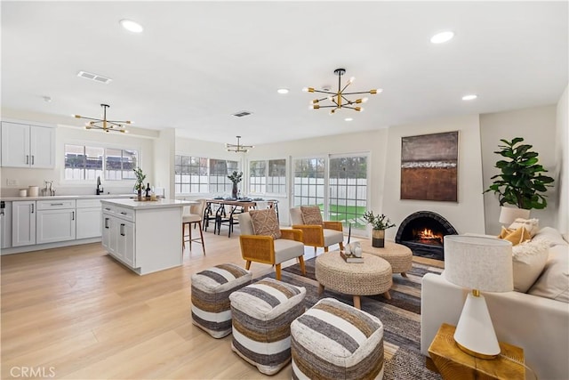 living room with a chandelier, light wood-type flooring, a wealth of natural light, and sink