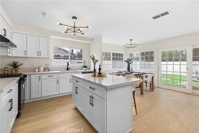 kitchen with pendant lighting, light hardwood / wood-style floors, stainless steel range with gas cooktop, and a notable chandelier