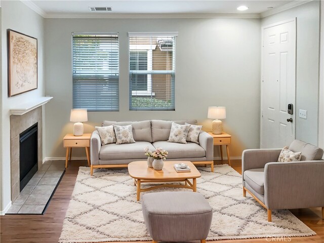 living room with hardwood / wood-style floors, crown molding, and a tiled fireplace