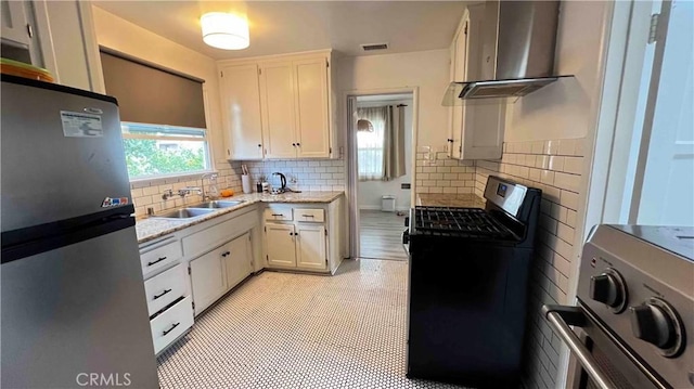 kitchen with black gas range, white cabinetry, stainless steel refrigerator, wall chimney exhaust hood, and sink