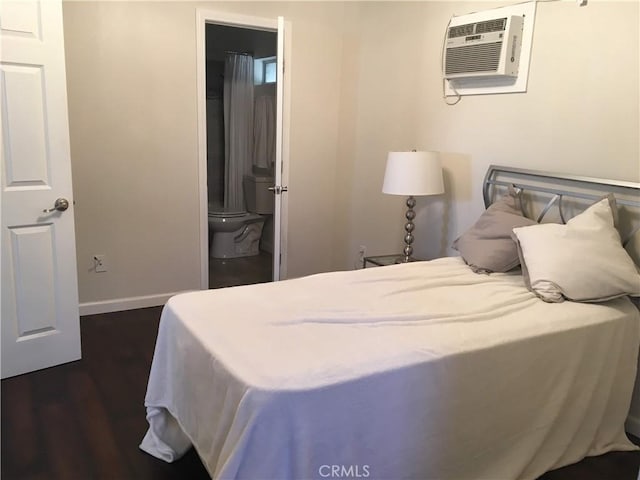 bedroom with a wall mounted air conditioner, dark hardwood / wood-style floors, and connected bathroom