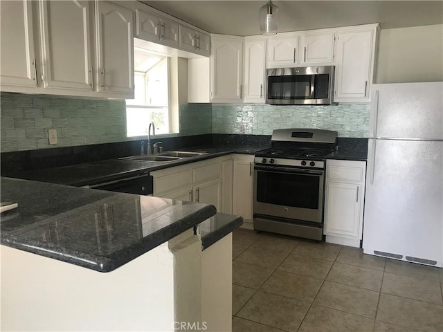 kitchen with sink, decorative backsplash, dark tile patterned floors, appliances with stainless steel finishes, and white cabinetry