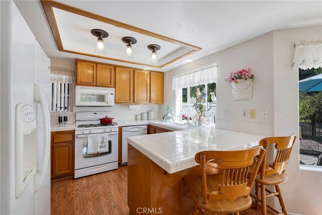 kitchen featuring tile countertops, white appliances, kitchen peninsula, and a tray ceiling