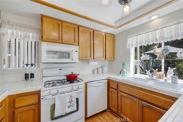 kitchen with tile countertops, white appliances, sink, and light hardwood / wood-style flooring