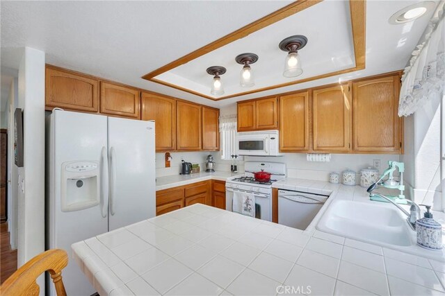 kitchen featuring kitchen peninsula, white appliances, a raised ceiling, and tile counters