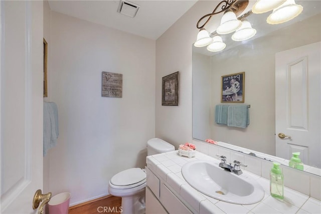 half bathroom with visible vents, toilet, wood finished floors, an inviting chandelier, and vanity