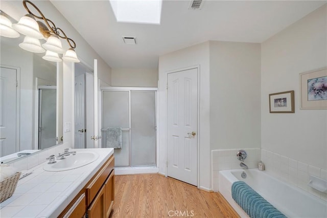 full bath featuring a skylight, a shower stall, vanity, and wood finished floors