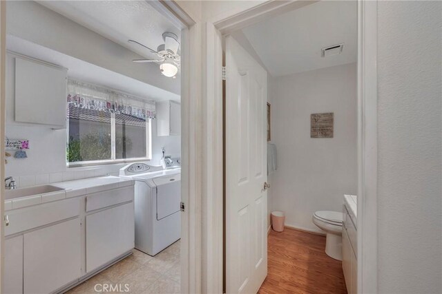 bathroom with ceiling fan, sink, washing machine and dryer, wood-type flooring, and toilet