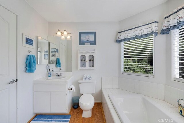 bathroom featuring vanity, tiled bath, toilet, and hardwood / wood-style flooring