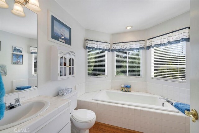 bathroom featuring tiled tub, vanity, wood-type flooring, and toilet