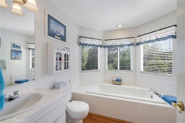 bathroom featuring toilet, wood finished floors, a garden tub, vanity, and recessed lighting