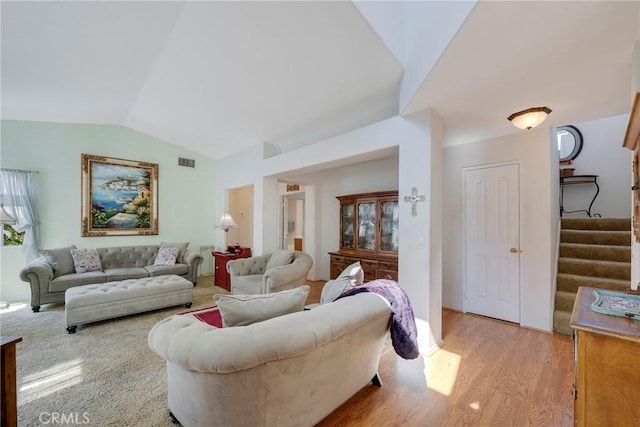 living area with stairs, visible vents, vaulted ceiling, and wood finished floors