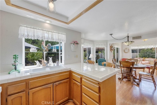 kitchen featuring a raised ceiling, visible vents, a sink, light wood-type flooring, and a peninsula