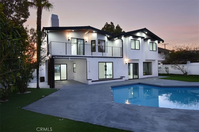 back house at dusk with a patio area, a balcony, a fenced in pool, and a yard