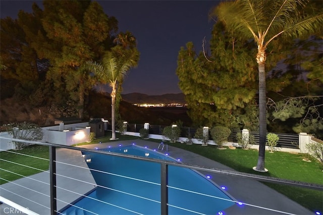 pool at night featuring a mountain view and a yard