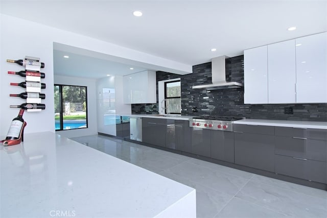 kitchen with decorative backsplash, appliances with stainless steel finishes, sink, wall chimney range hood, and white cabinets