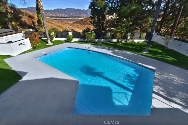 view of swimming pool featuring a lawn, a mountain view, and a shed