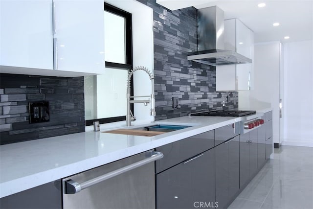 kitchen with decorative backsplash, appliances with stainless steel finishes, sink, wall chimney range hood, and white cabinets