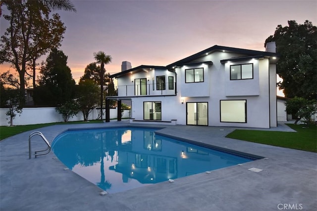 pool at dusk featuring a patio and a lawn