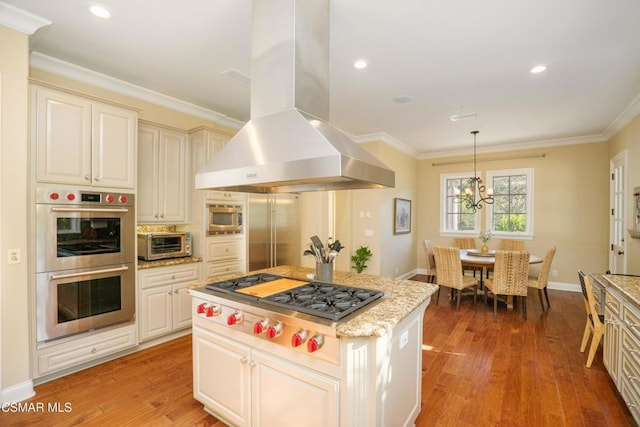 kitchen with decorative light fixtures, light wood-type flooring, stainless steel appliances, and wall chimney range hood