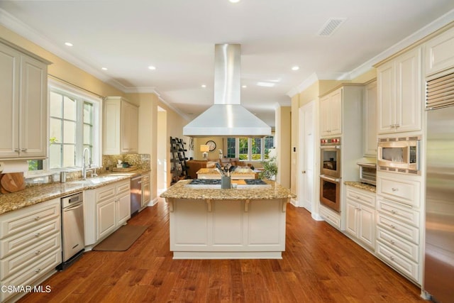 kitchen with built in appliances, cream cabinetry, a kitchen island, wood-type flooring, and island exhaust hood