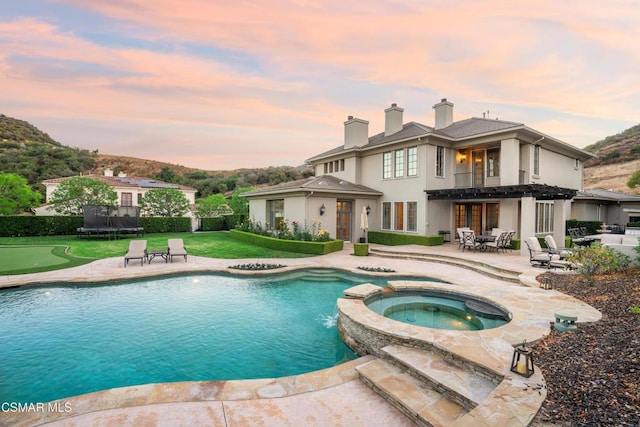 back house at dusk with a swimming pool with hot tub, a patio, and a trampoline