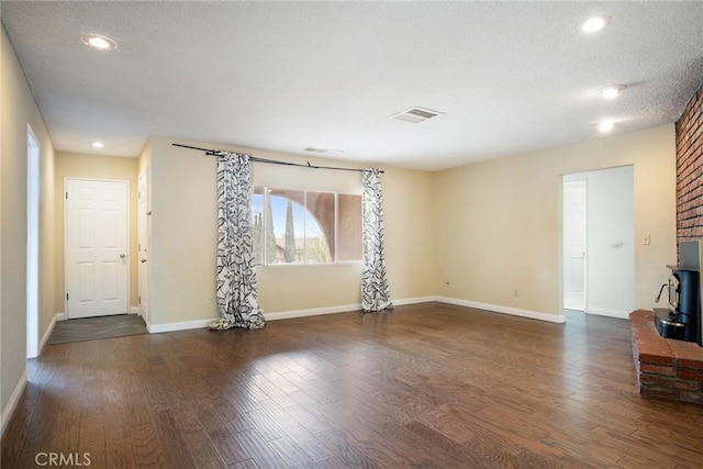 unfurnished living room featuring a textured ceiling, a wood stove, and dark wood-type flooring