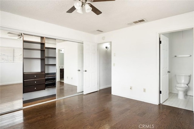 unfurnished bedroom featuring ceiling fan, dark wood-type flooring, ensuite bathroom, a textured ceiling, and a closet