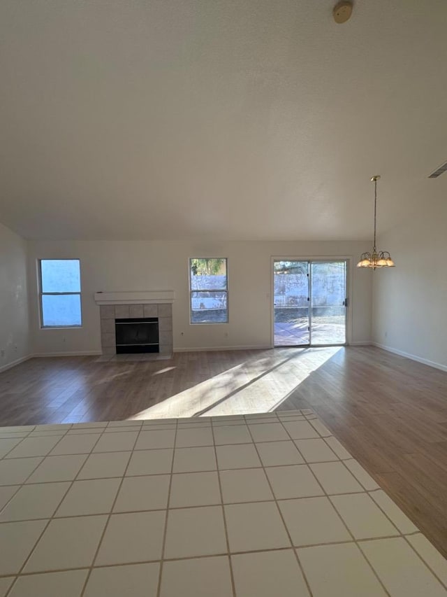 unfurnished living room featuring light hardwood / wood-style floors, a tile fireplace, and an inviting chandelier