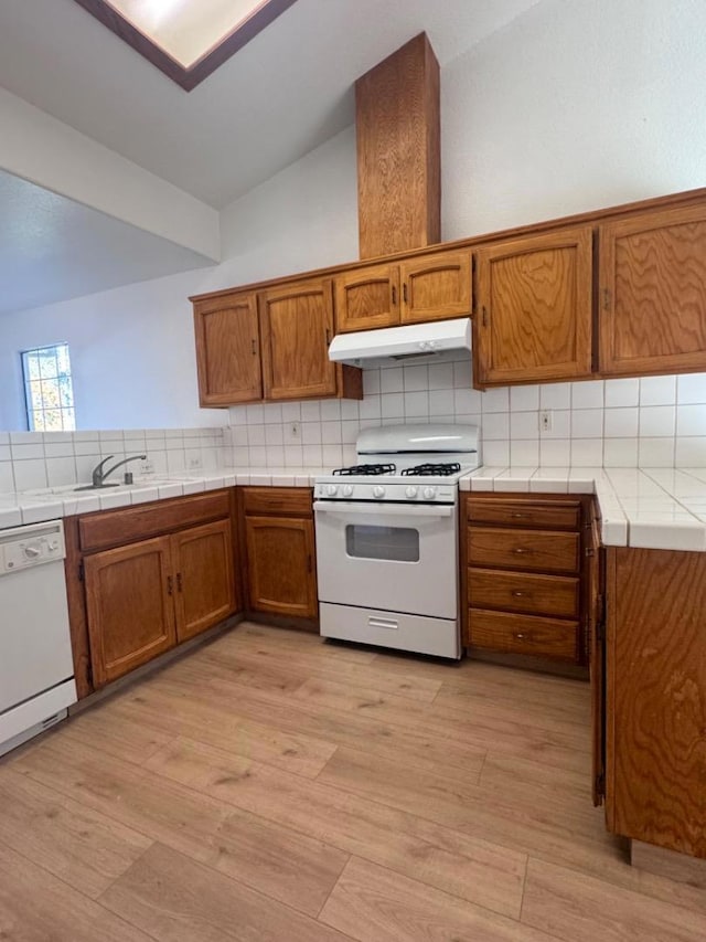 kitchen featuring tile countertops, decorative backsplash, white appliances, vaulted ceiling, and sink