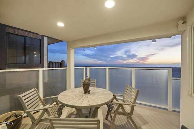 balcony at dusk featuring a water view