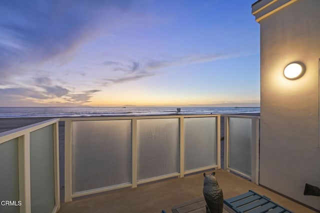 balcony at dusk featuring a water view and a beach view