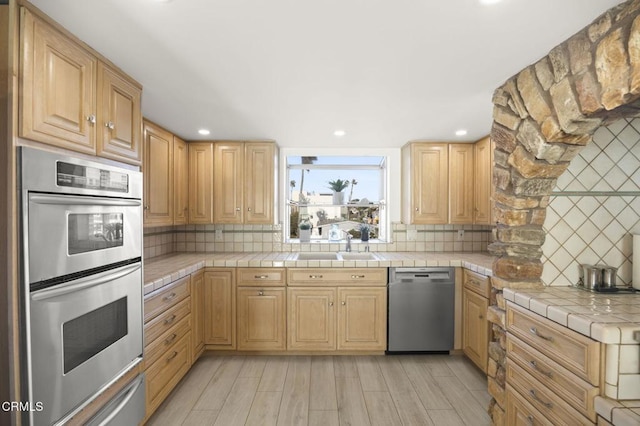 kitchen with tile countertops, decorative backsplash, light hardwood / wood-style flooring, and appliances with stainless steel finishes