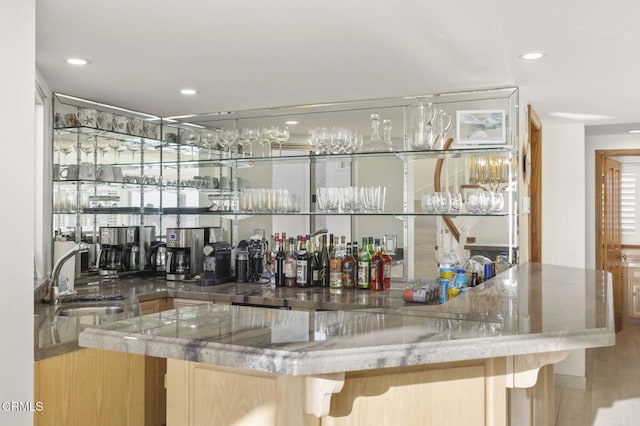 bar with sink, light hardwood / wood-style floors, and stone countertops