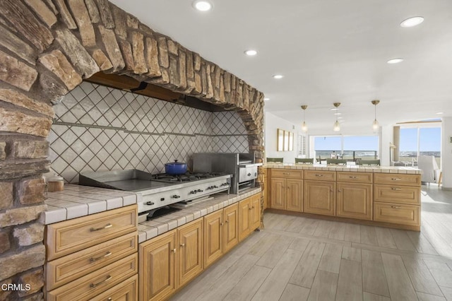 kitchen with tile counters, hanging light fixtures, gas stovetop, light hardwood / wood-style flooring, and decorative backsplash